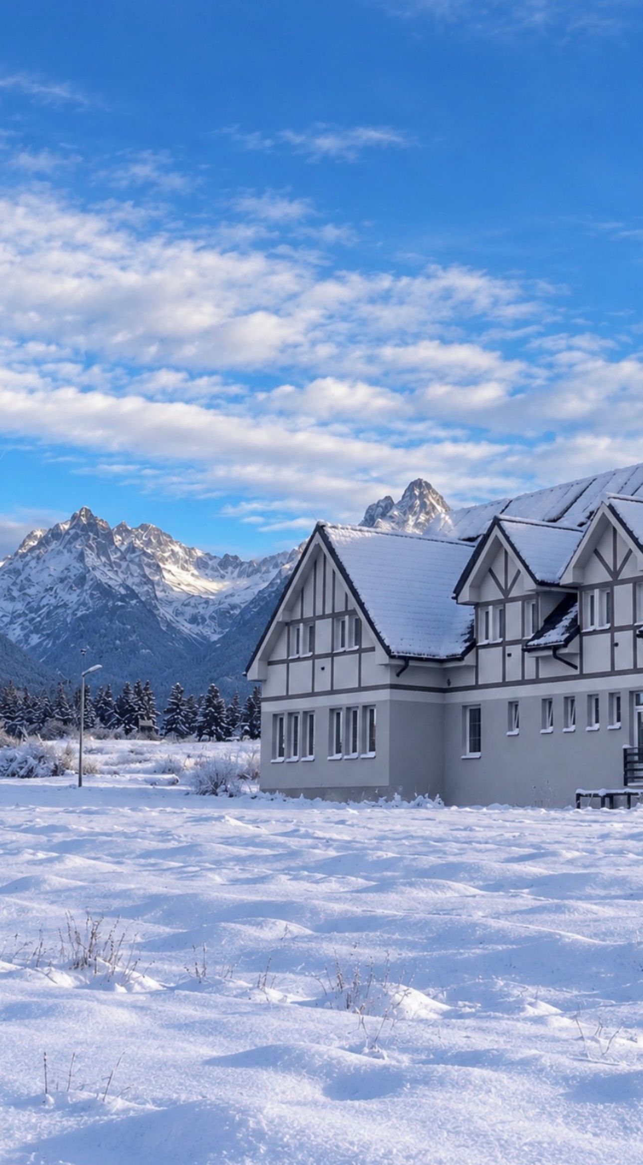 A large, multi-story building with a symmetrical facade, set against a backdrop of snow-covered mountains and a clear sky.