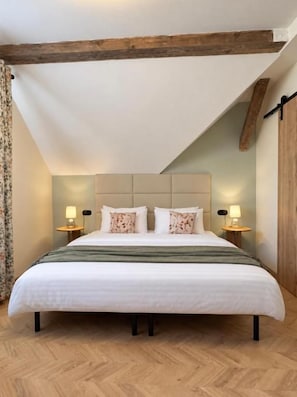 Een slaapkamer met een groot bed, houten balken, twee bedlampen en een visgraat vloerpatroon.