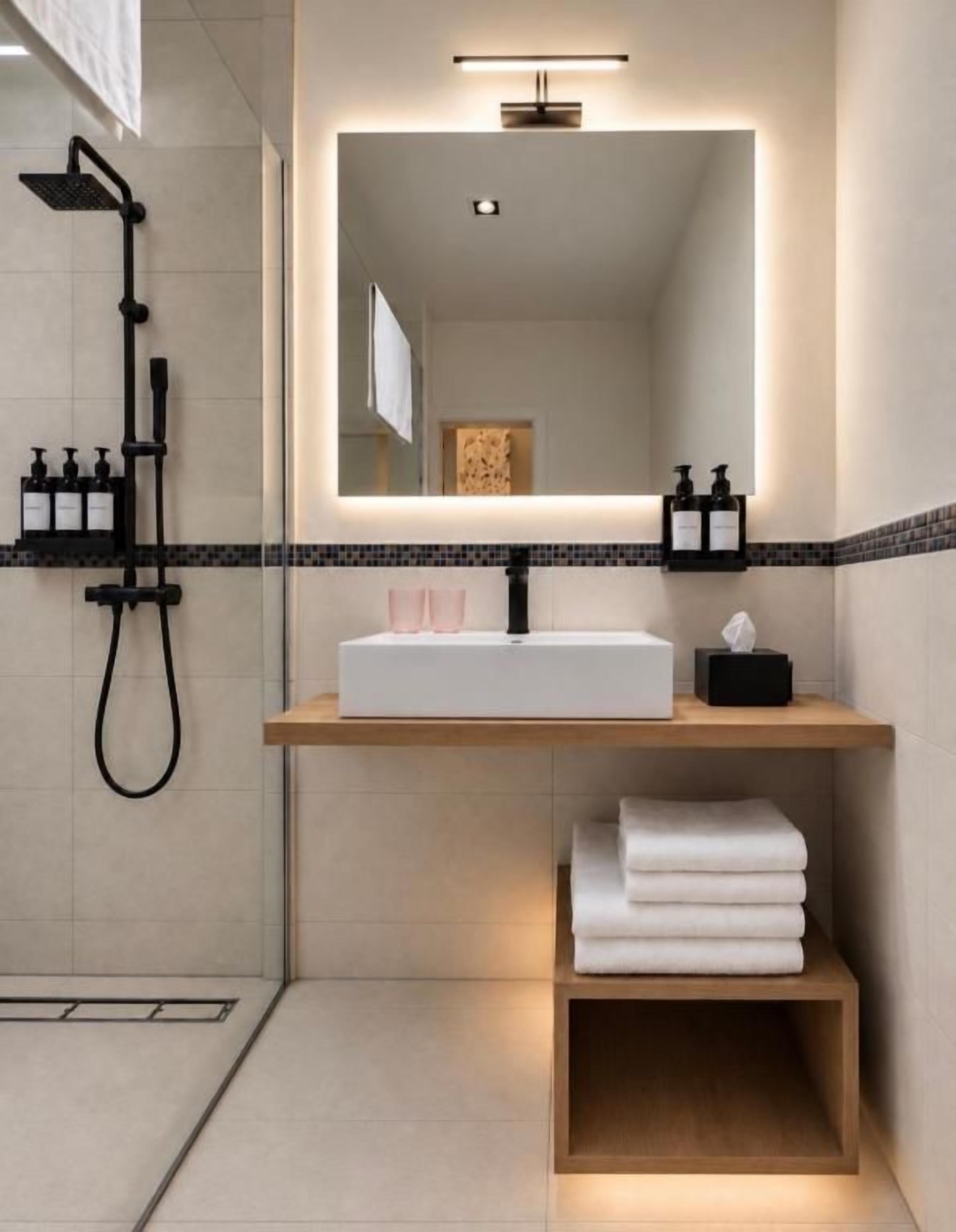 Un bagno moderno con un grande specchio, un lavandino bianco, un soffione doccia estraibile e asciugamani ordinatamente piegati.