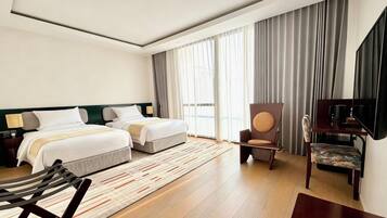Habitación de hotel con dos camas, televisión, una silla y un ventanal con cortinas.