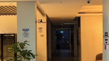 Un vestíbulo de hotel con una recepción, una planta en maceta, un cartel informativo y una cámara de seguridad.