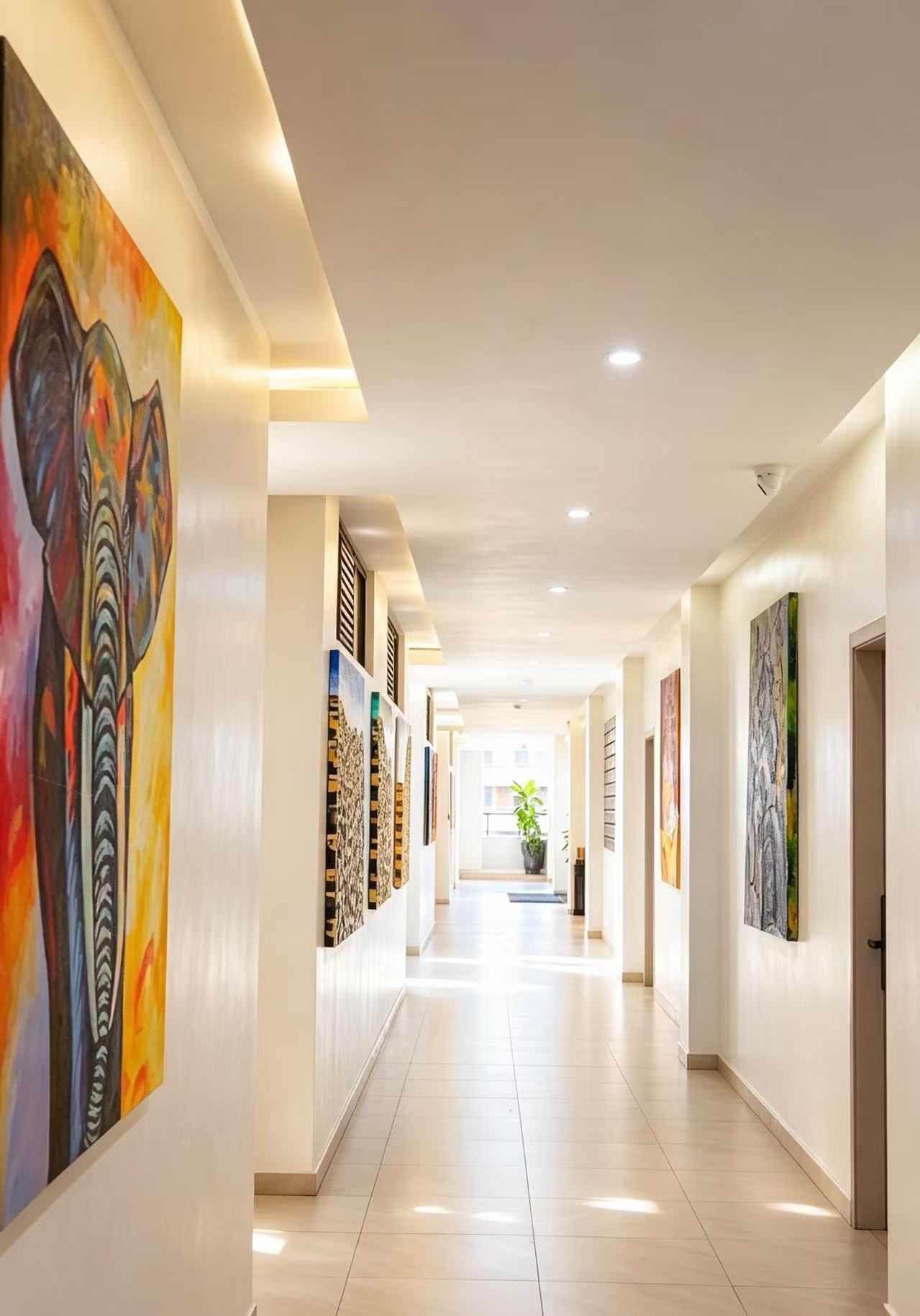 Een hotelgang met kunstwerken aan de muren, een betegelde vloer en een plafond met inbouwverlichting.