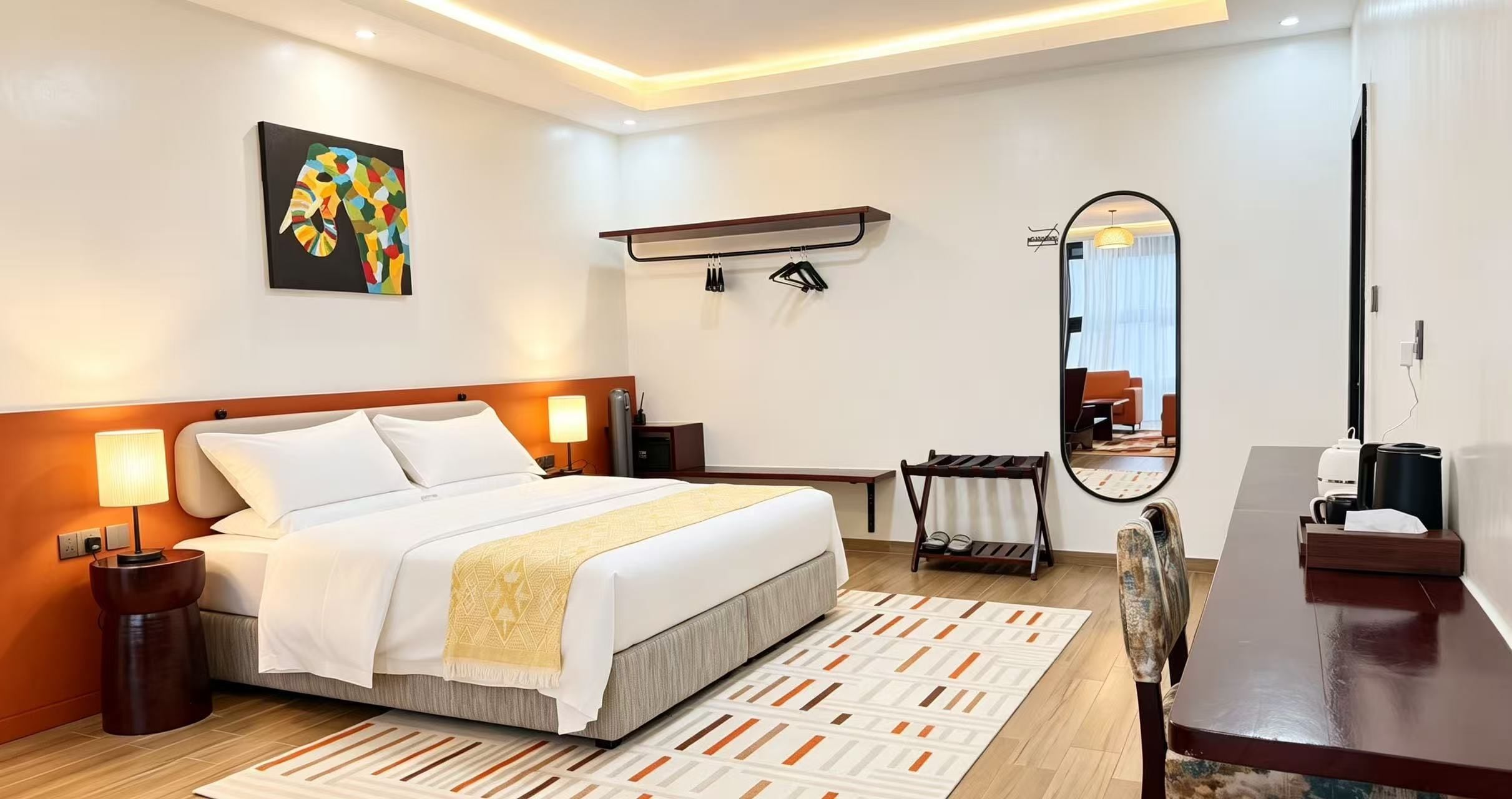 A hotel room with a bed, bedside lamps, a mirror, a desk, and a radiator.
