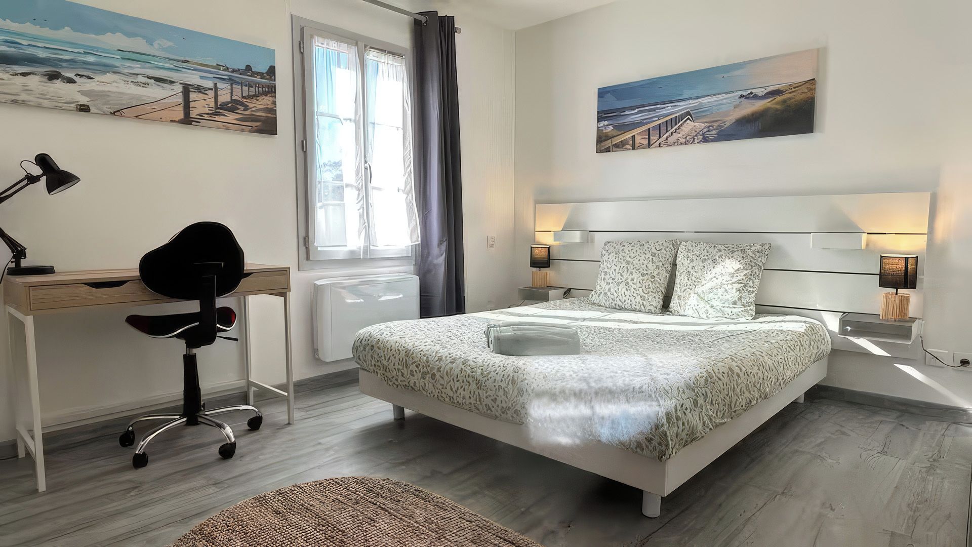 Un dormitorio con cama, escritorio, silla y dos cuadros.