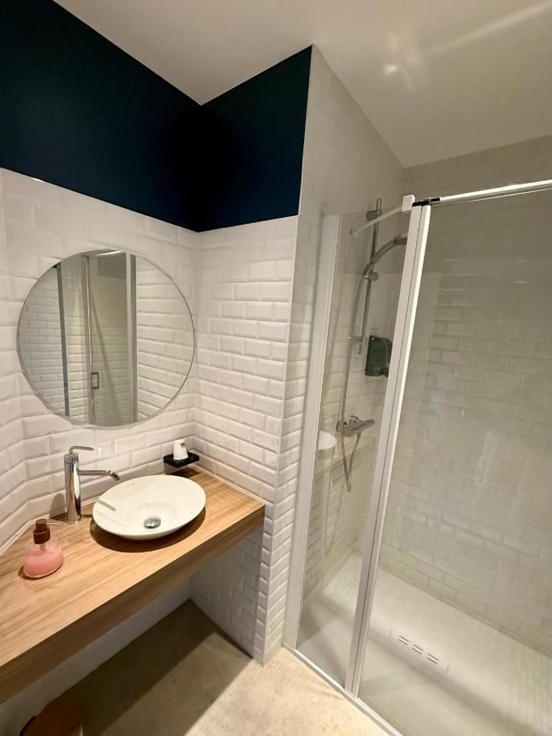 Une salle de bain avec un lavabo blanc, un miroir rond et une cabine de douche en verre.