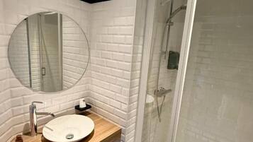 Une salle de bain avec un lavabo blanc, un miroir rond et une cabine de douche en verre.