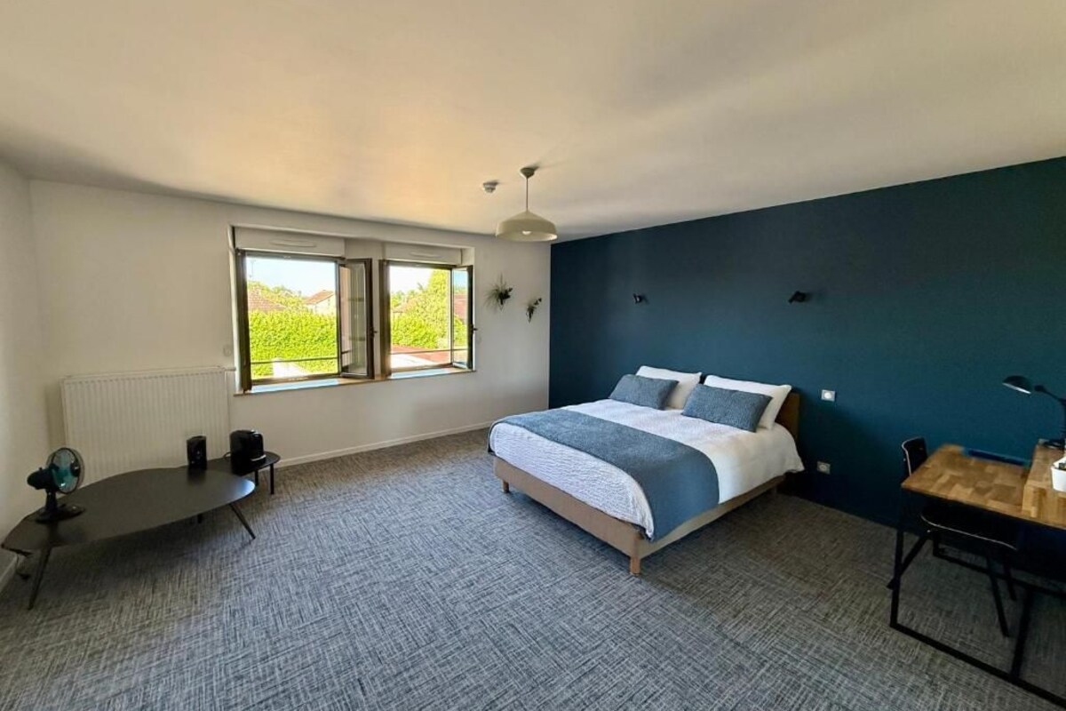 A bedroom with a bed, a desk, a chair, a radiator, and a window.
