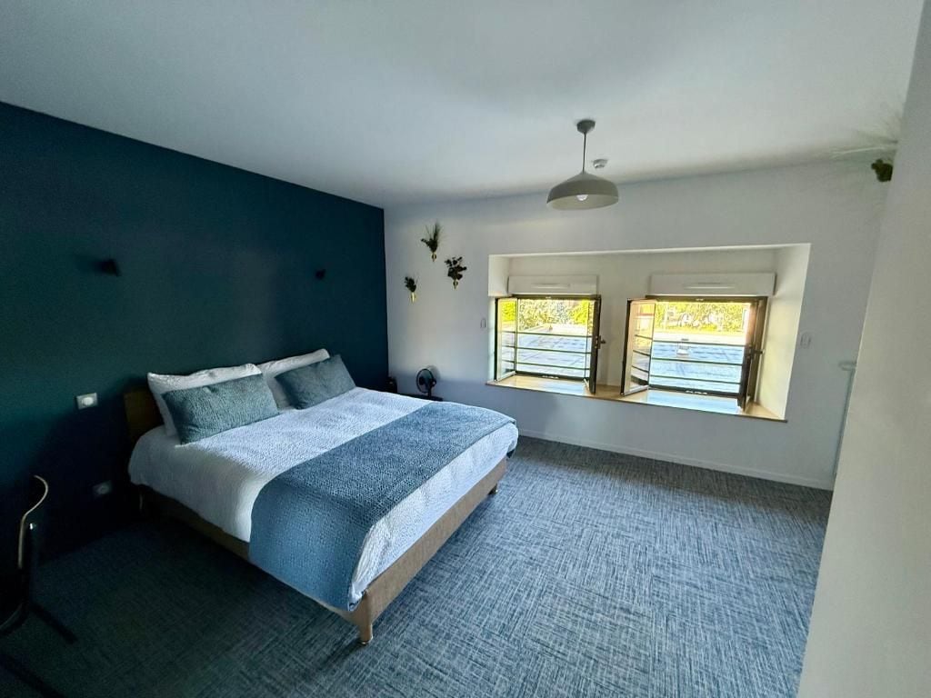 Een slaapkamer met een bed, een stoel, een bureau en twee ramen met uitzicht.