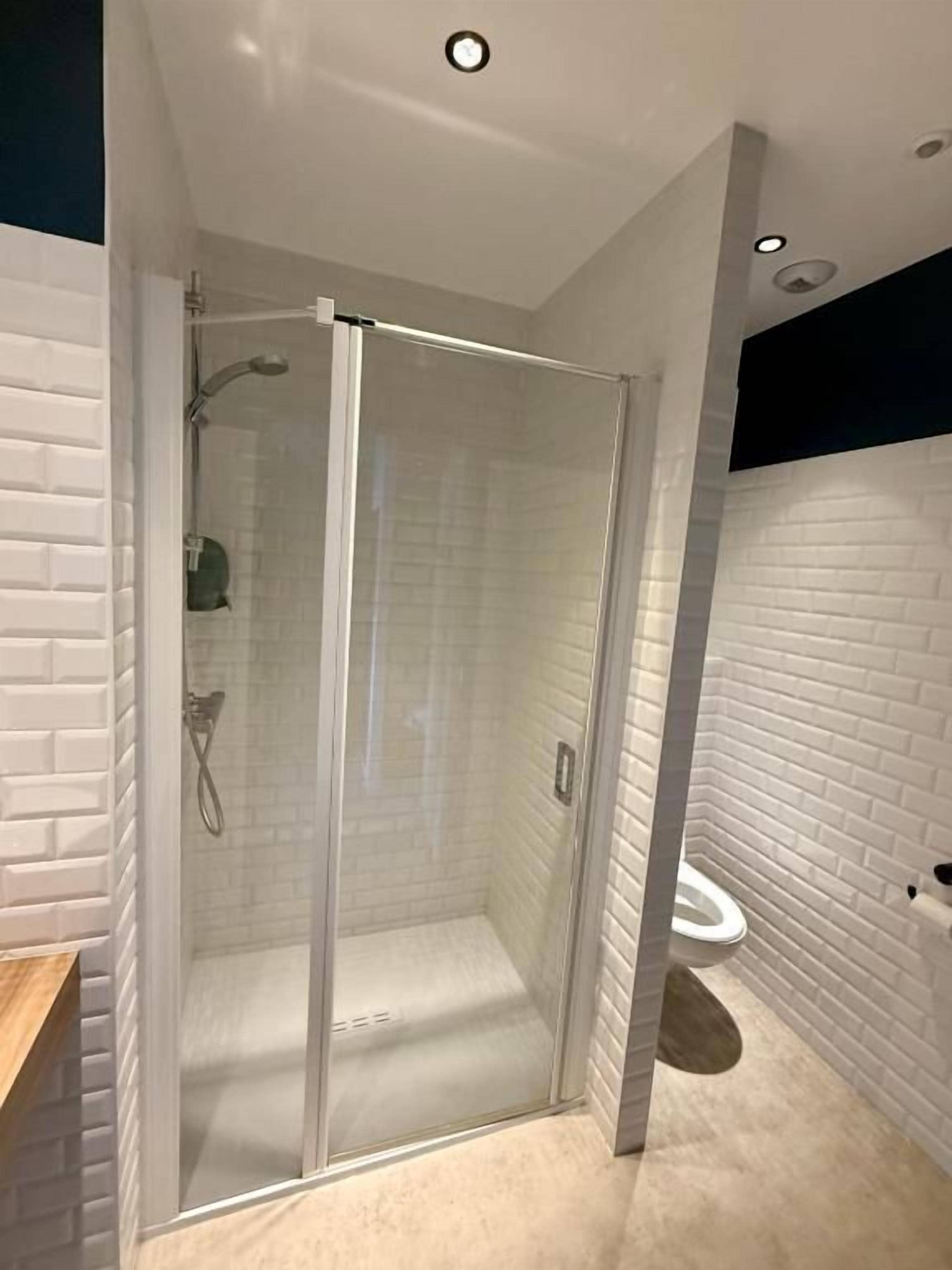 Ein modernes Badezimmer mit einer gläsernen Duschkabine, weißen Ziegelwänden und einem sichtbaren WC.
