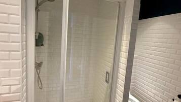 Ein modernes Badezimmer mit einer gläsernen Duschkabine, weißen Ziegelwänden und einem sichtbaren WC.