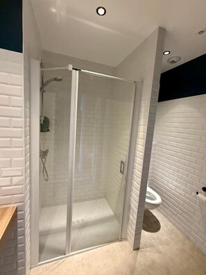 A modern bathroom with a glass-enclosed shower, white brick walls, and a visible toilet. - Le Billot (Bologne)
