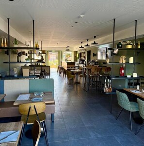 A modern restaurant with high tables and booths, a bar area, and shelves with bottles. - Le Billot (Bologne)