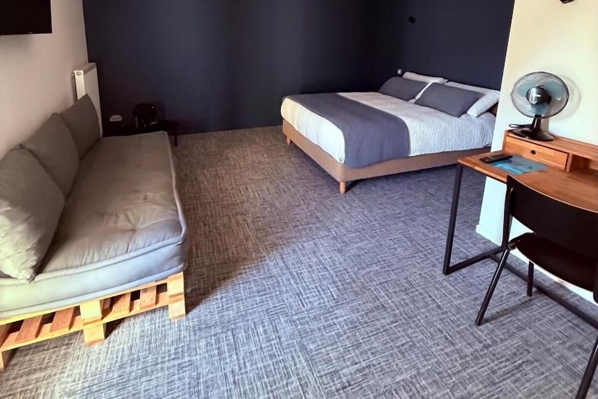 A compact bedroom with a bed, a sofa, a desk, and a chair.