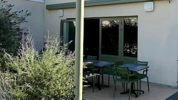 A building with a patio area featuring a table and chairs, a green door, and a window.