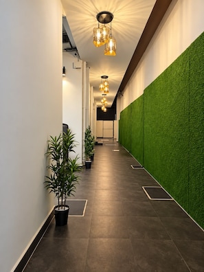 A corridor with artificial grass walls, potted plants, and modern lighting fixtures. - Hotel Oasis (Coimbatore)
