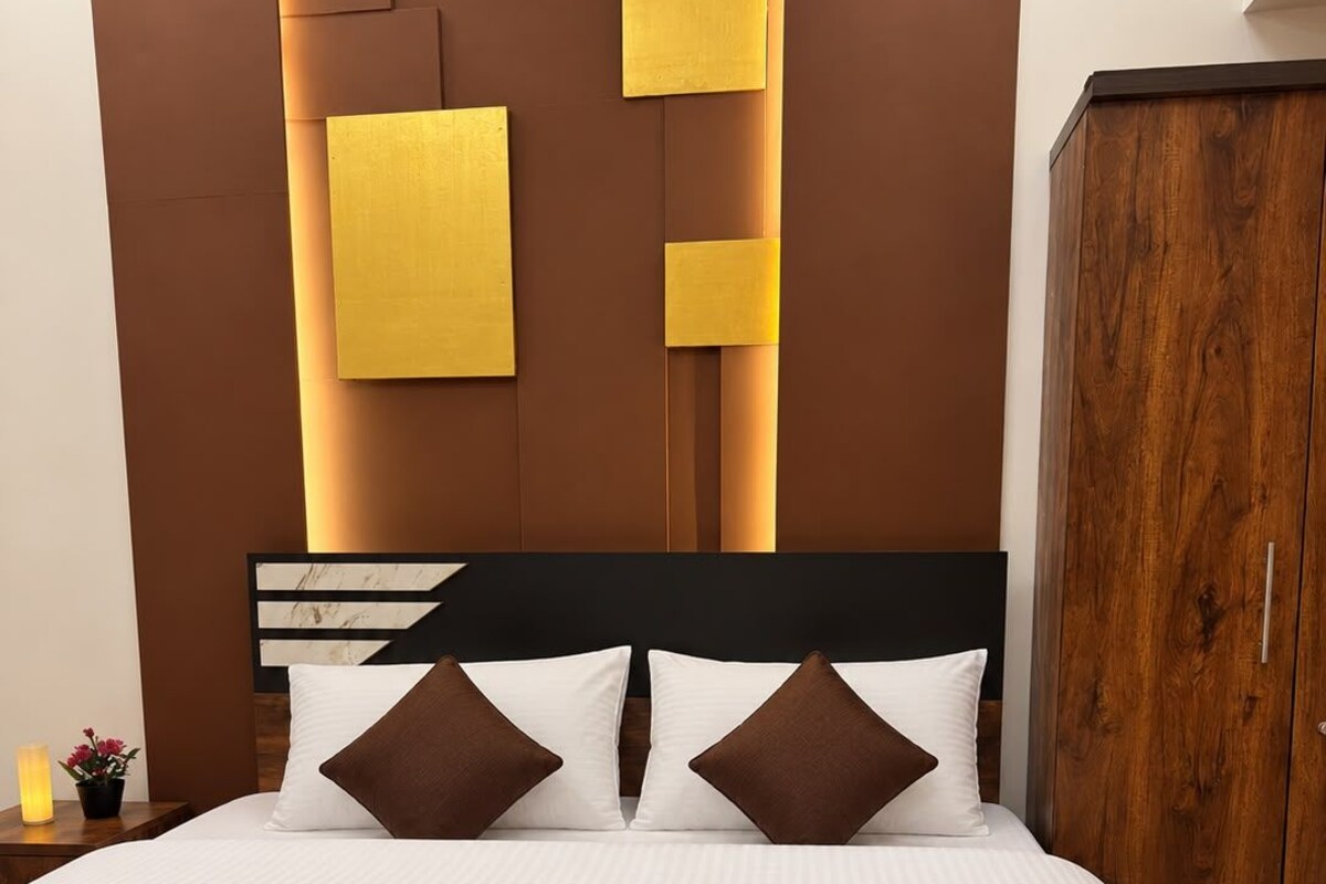 A bed with white bedding and two brown pillows, a wooden wardrobe, and a wall with geometric light fixtures.