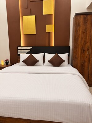 A bed with white bedding and two brown pillows, a wooden wardrobe, and a wall with geometric light fixtures. - Hotel Oasis (Coimbatore)