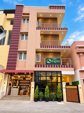 Un hotel de varios pisos con un cartel llamativo que dice 'Hotel Oasis' y una entrada visible con un toldo rojo.