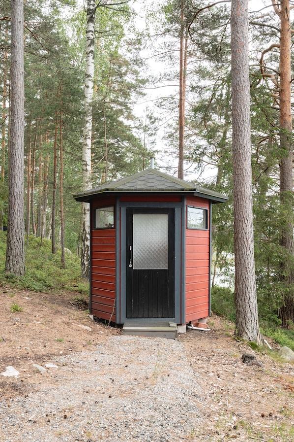 A small cabin with a black door and windows, surrounded by tall trees in a forest.