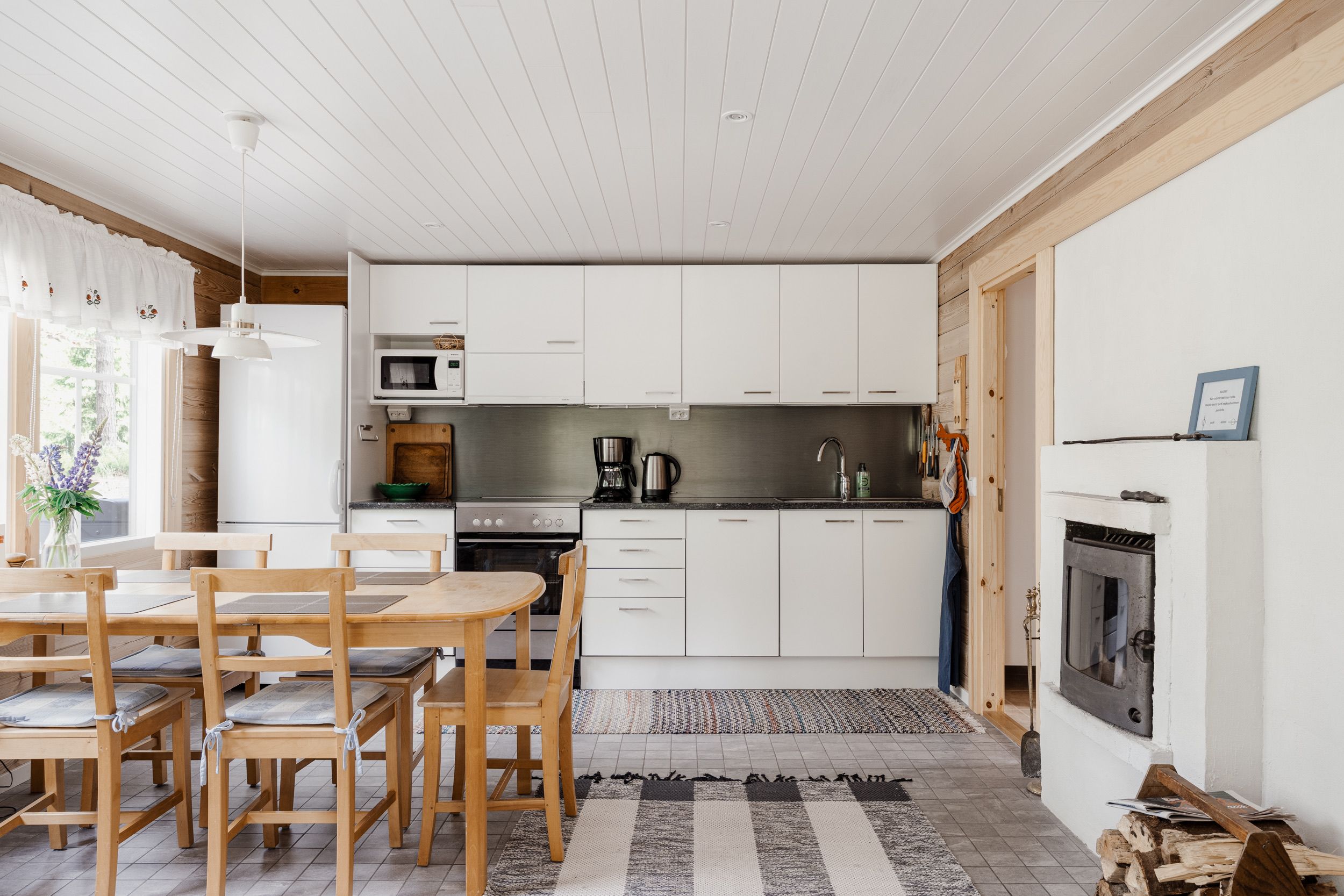 Une cuisine moderne avec des meubles blancs, un coin repas avec des meubles en bois et une cheminée.