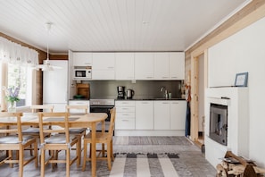 A modern kitchen with white cabinets, a dining area with wooden furniture, and a fireplace. - Villa Casanova - Private Seaside Cabin (Porvoo)