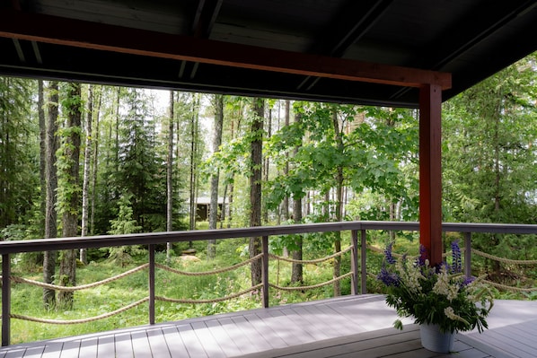 A wooden deck with a rope barrier, overlooking a forested area with tall trees.