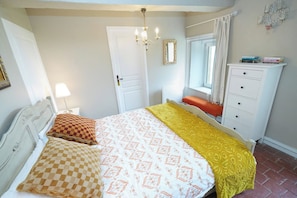 A bedroom with a bed, a nightstand, a dresser, a window with curtains, and a chandelier. - Vrbo Property (Onlay)