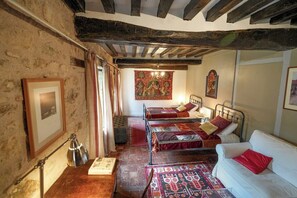 A traditional room with exposed wooden beams, a bed with a red and white bedspread, a white sofa, and a tapestry on the wall. - Vrbo Property (Onlay)