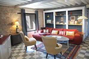 Un salon chaleureux avec un canapé rouge, deux fauteuils, une table basse et une bibliothèque.