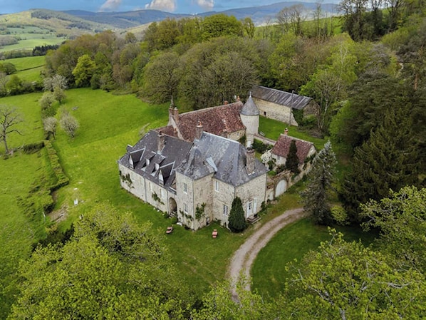 A stone building with a traditional roof, surrounded by lush green fields and trees. - Vrbo Property (Onlay)