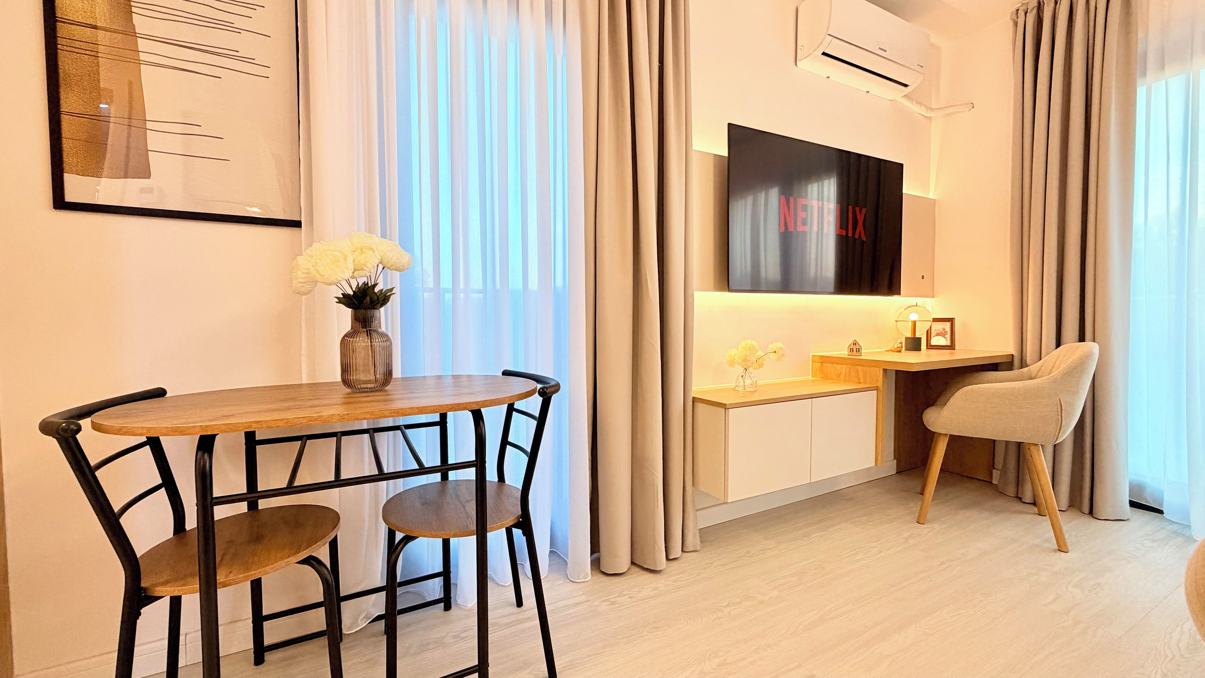 Una habitación moderna con una mesa de comedor, sillas, un escritorio pequeño, un televisor y una ventana con cortinas.