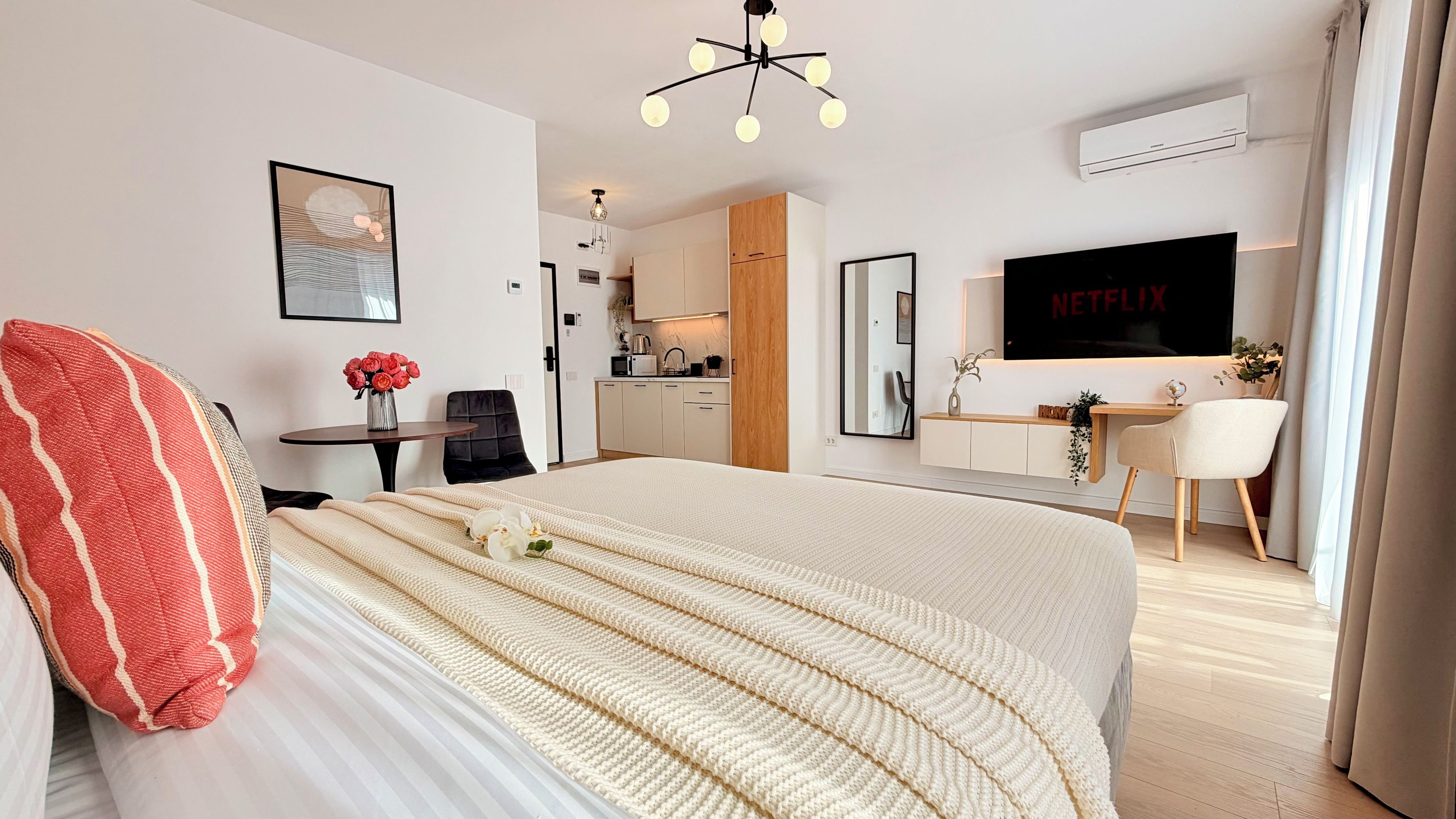 A hotel room with a bed, a desk, a TV, and a kitchenette.