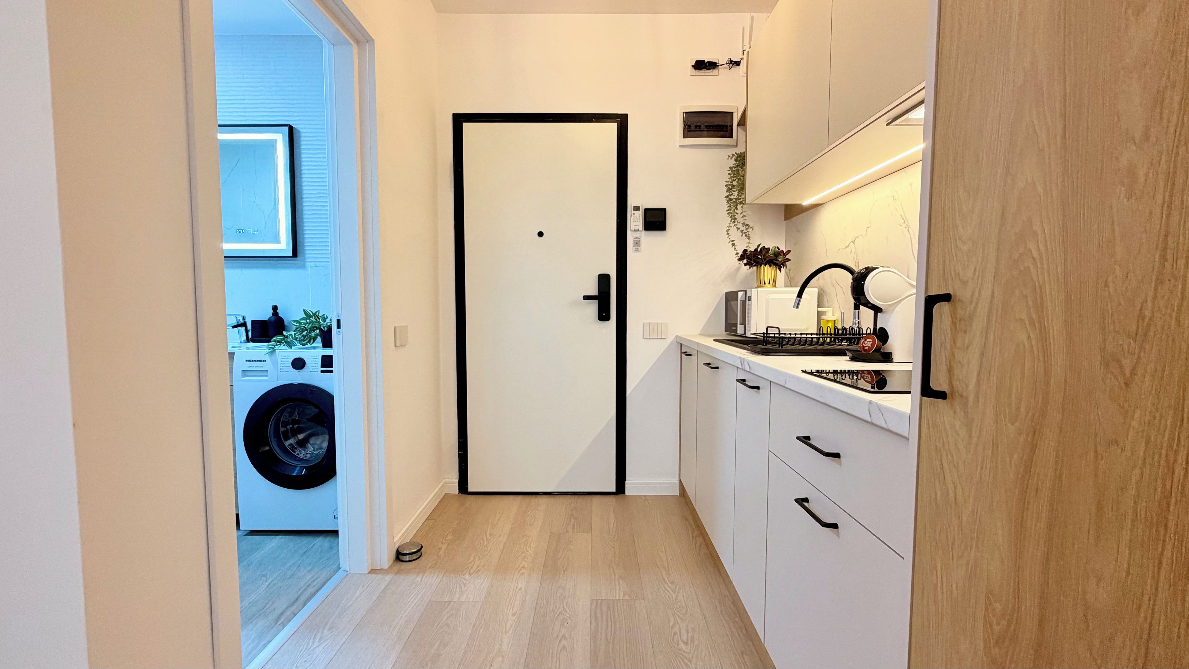 Cocina compacta con lavadora integrada, una puerta con picaporte y una encimera con lavamanos y varios electrodomésticos.