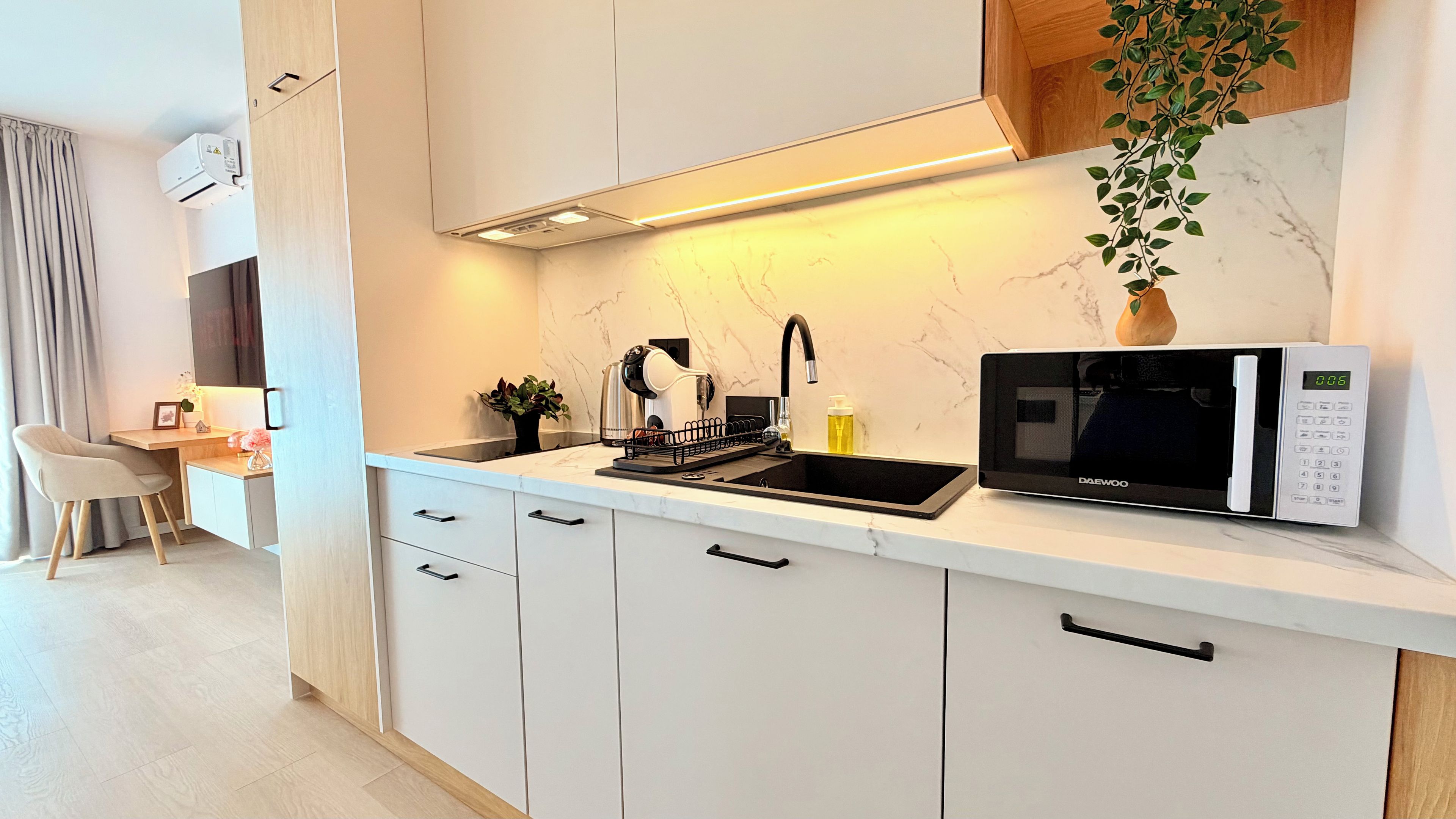 Una cocina moderna con microondas incorporado, un lavamanos y una pequeña zona de comedor con una silla y una mesa.