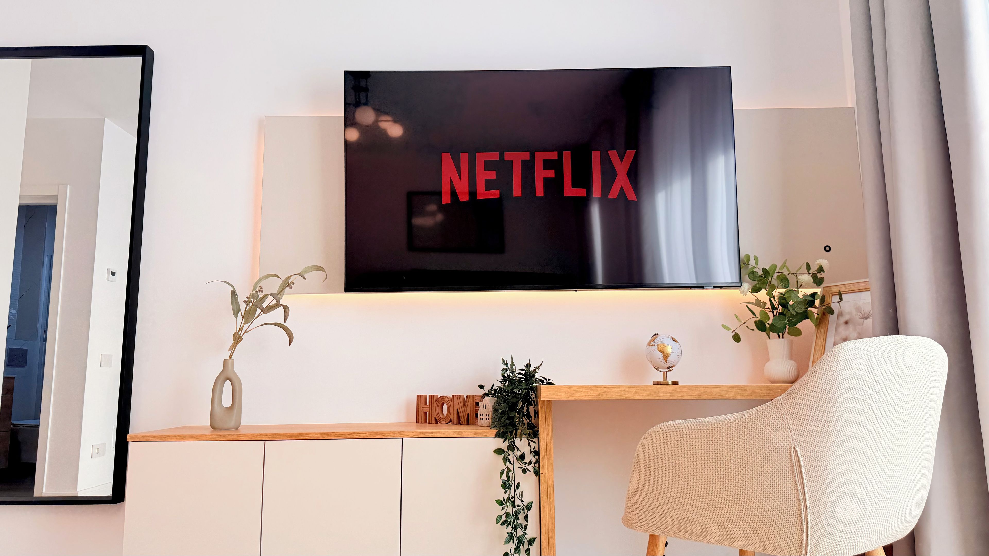 Una sala de estar moderna con un televisor de pantalla plana montado en la pared, una consola de madera, un sillón blanco y una planta en maceta.