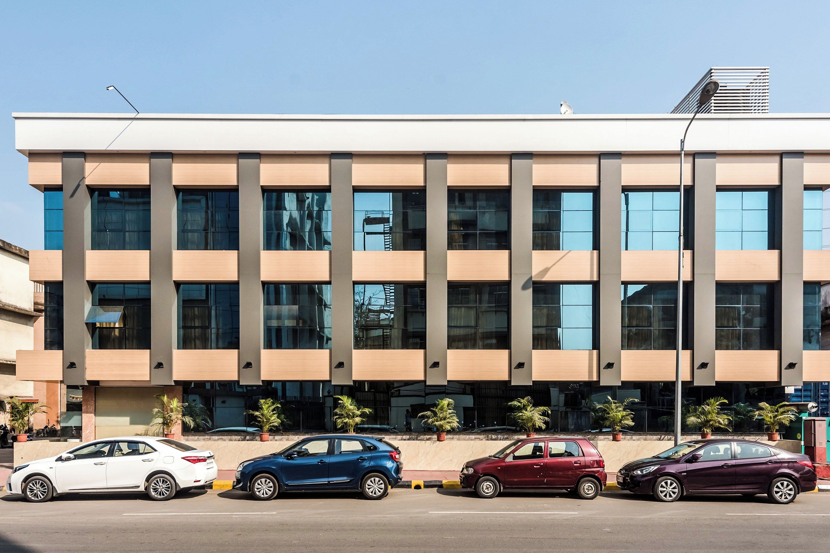 A modern building with a flat roof, large windows, and a parking area with several cars.
