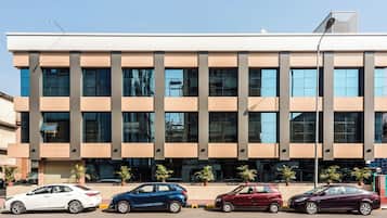 A modern building with a flat roof, large windows, and a parking area with several cars.