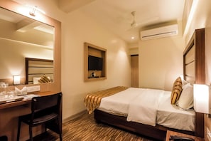 Una habitación de hotel con cama, escritorio, silla, espejo, ventilador de techo y aire acondicionado.