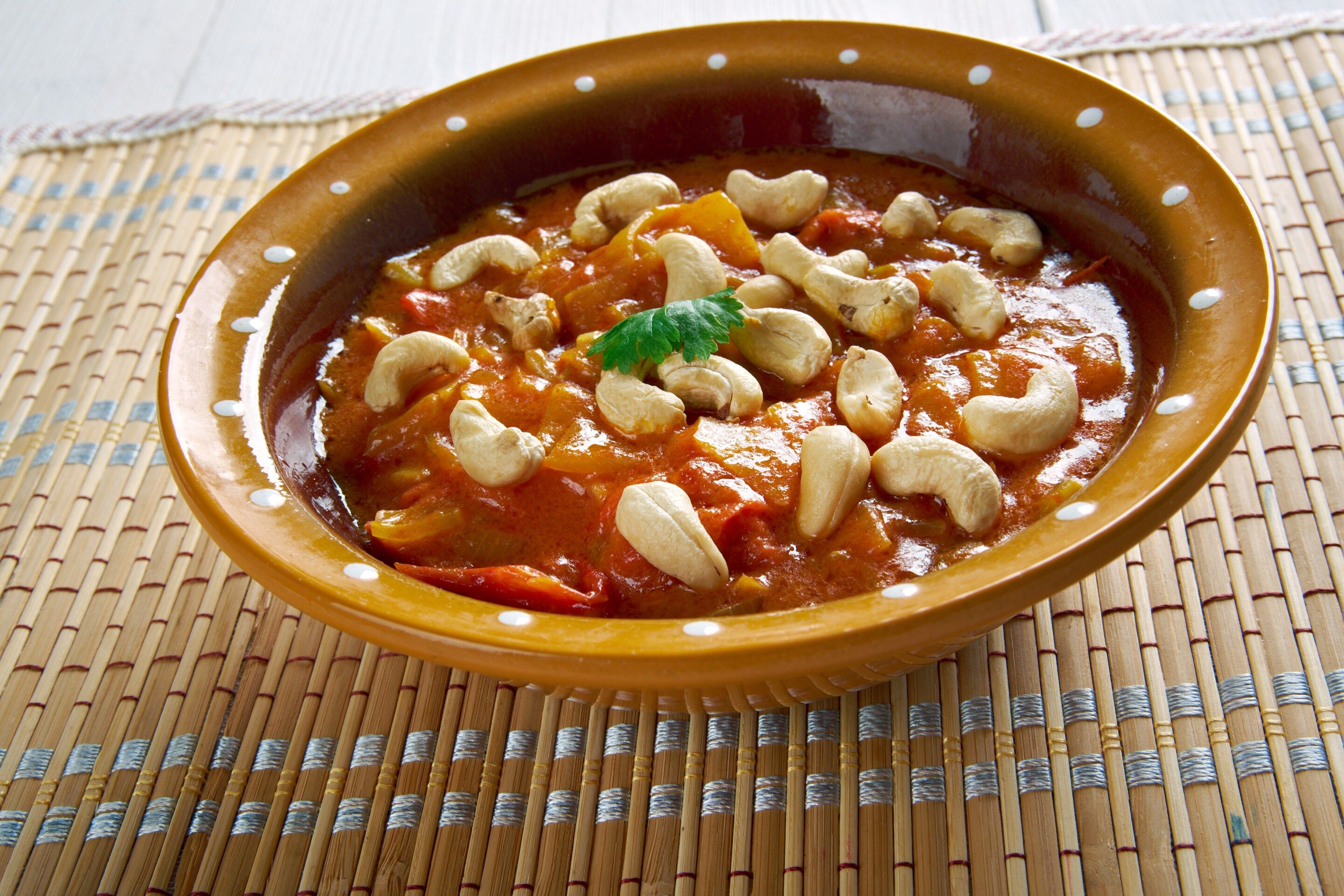A bowl of curry with cashews on a woven mat.