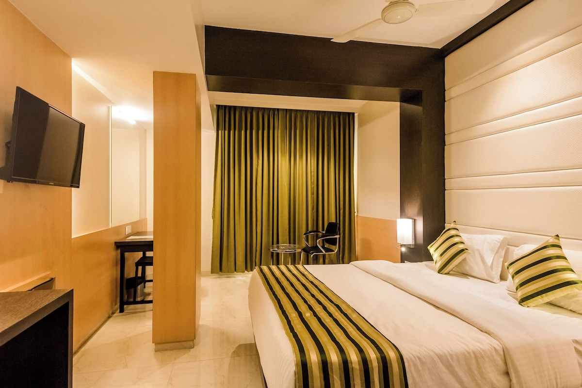 Una habitación de hotel con cama, escritorio, silla, televisor y cortina.