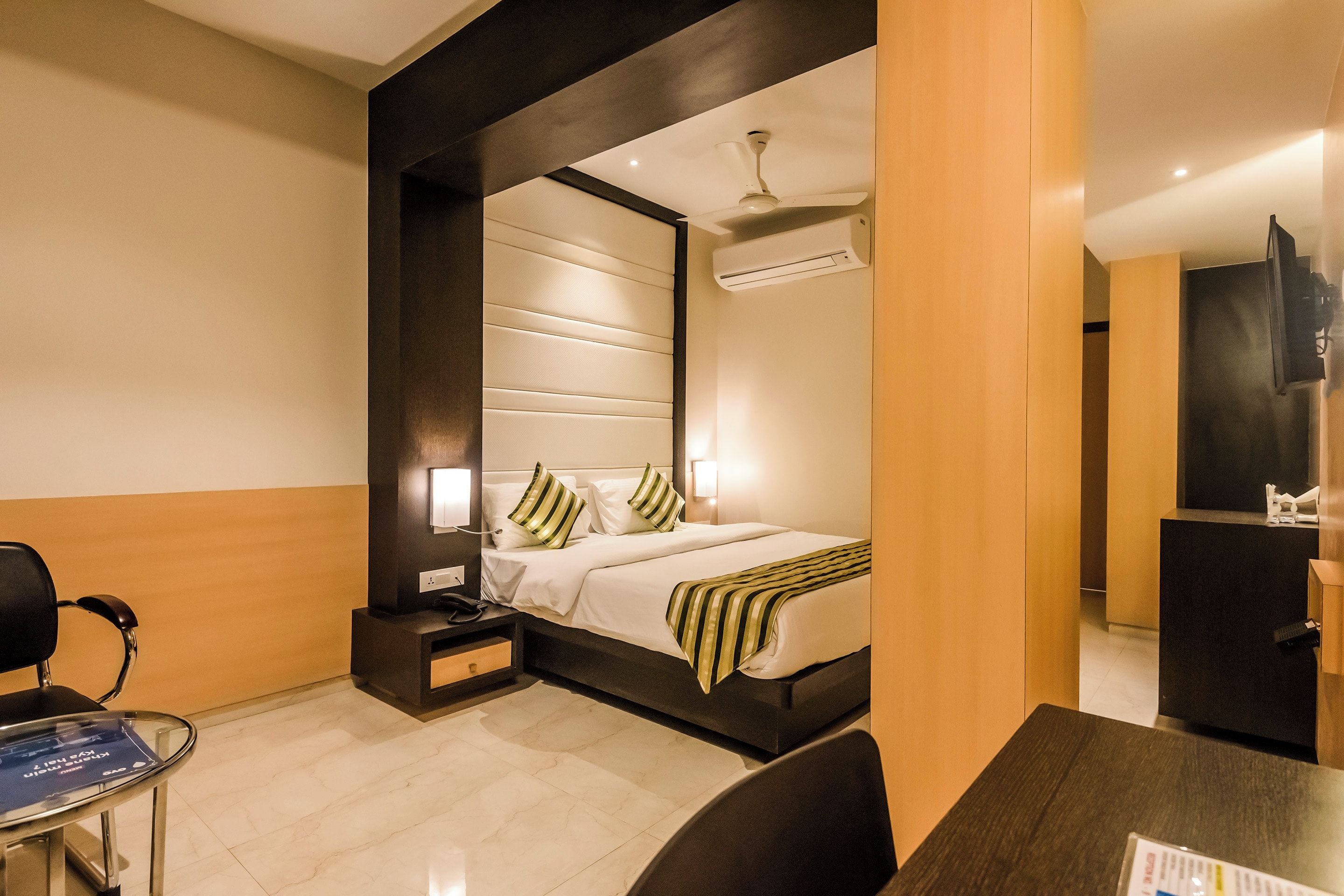 Una habitación de hotel con cama, mesita de noche, silla y escritorio con computadora.