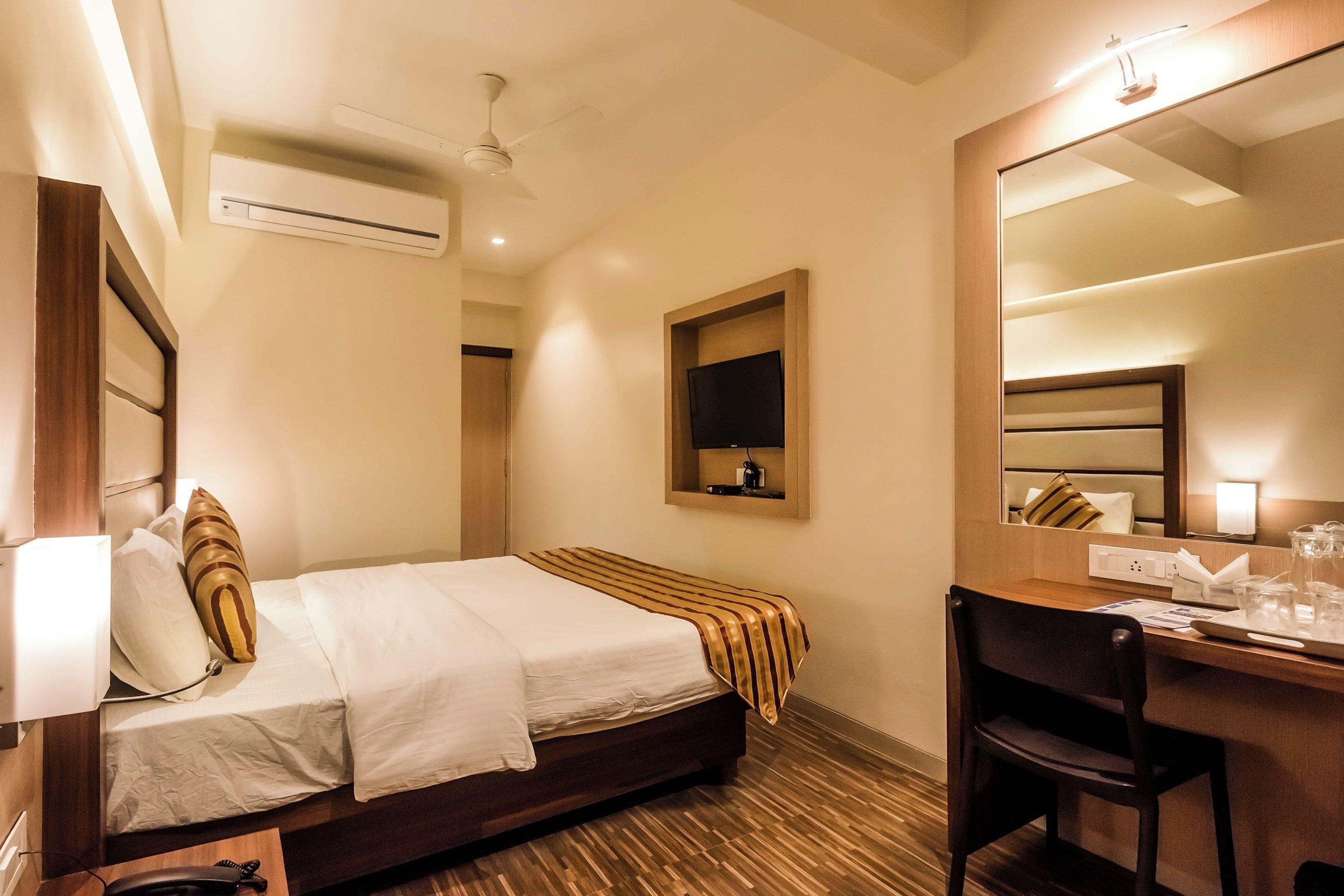 A hotel room with a bed, a desk, a chair, a television, and a mirror.