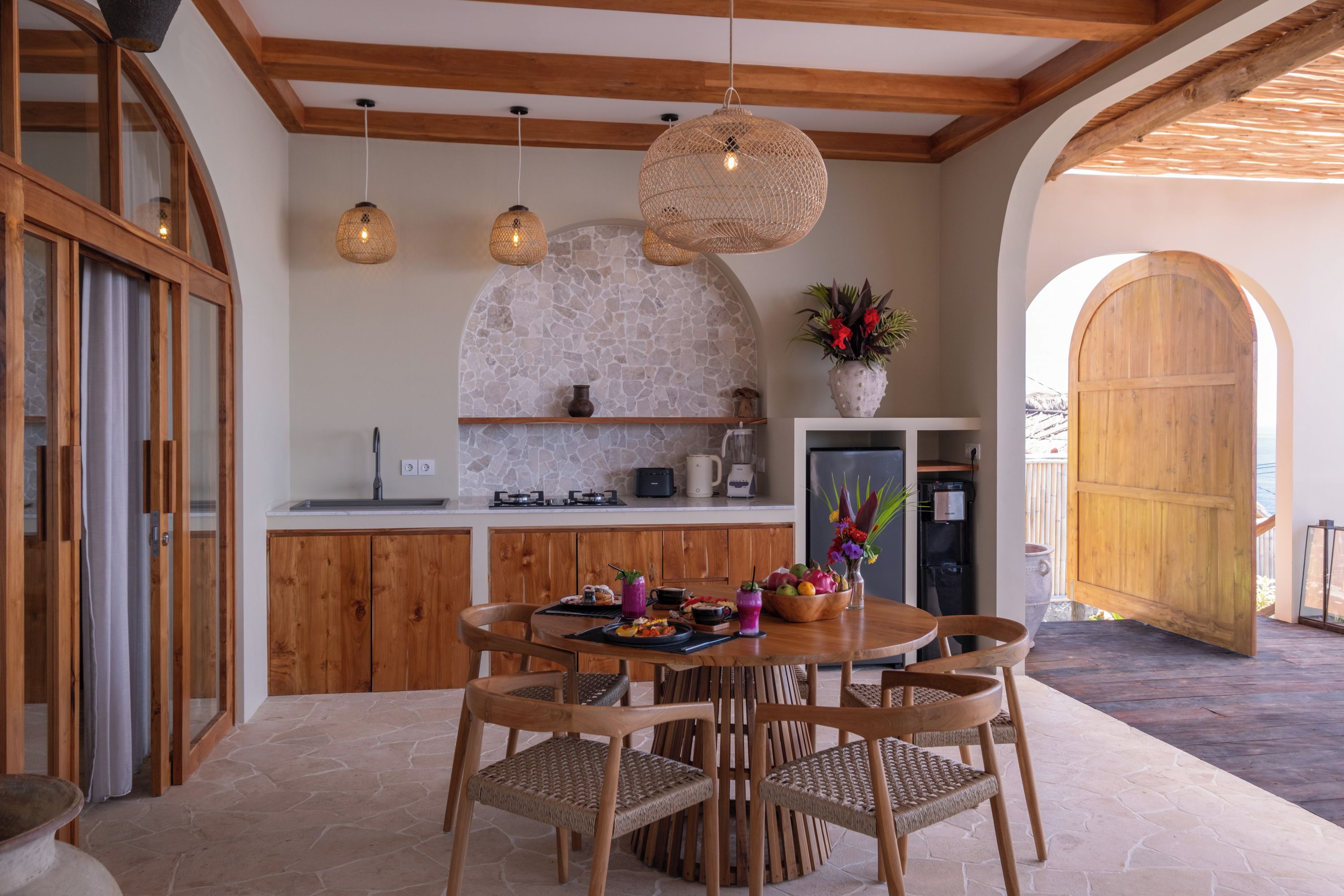 A kitchen with stone backsplash, wooden cabinets, and a dining area with wicker chairs.