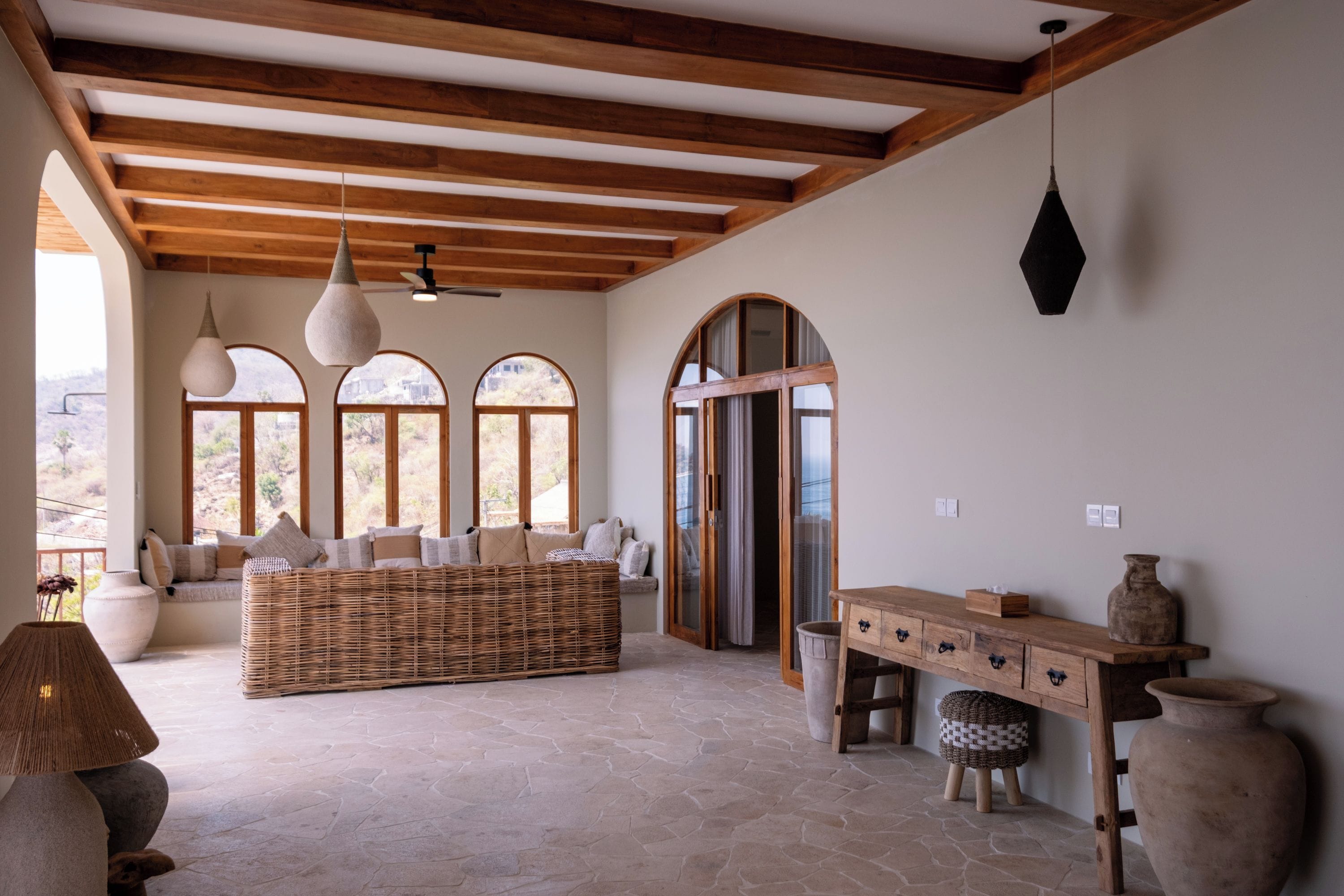 Una habitación amplia con un sofá grande de mimbre, una mesa de madera y suelo de piedra.