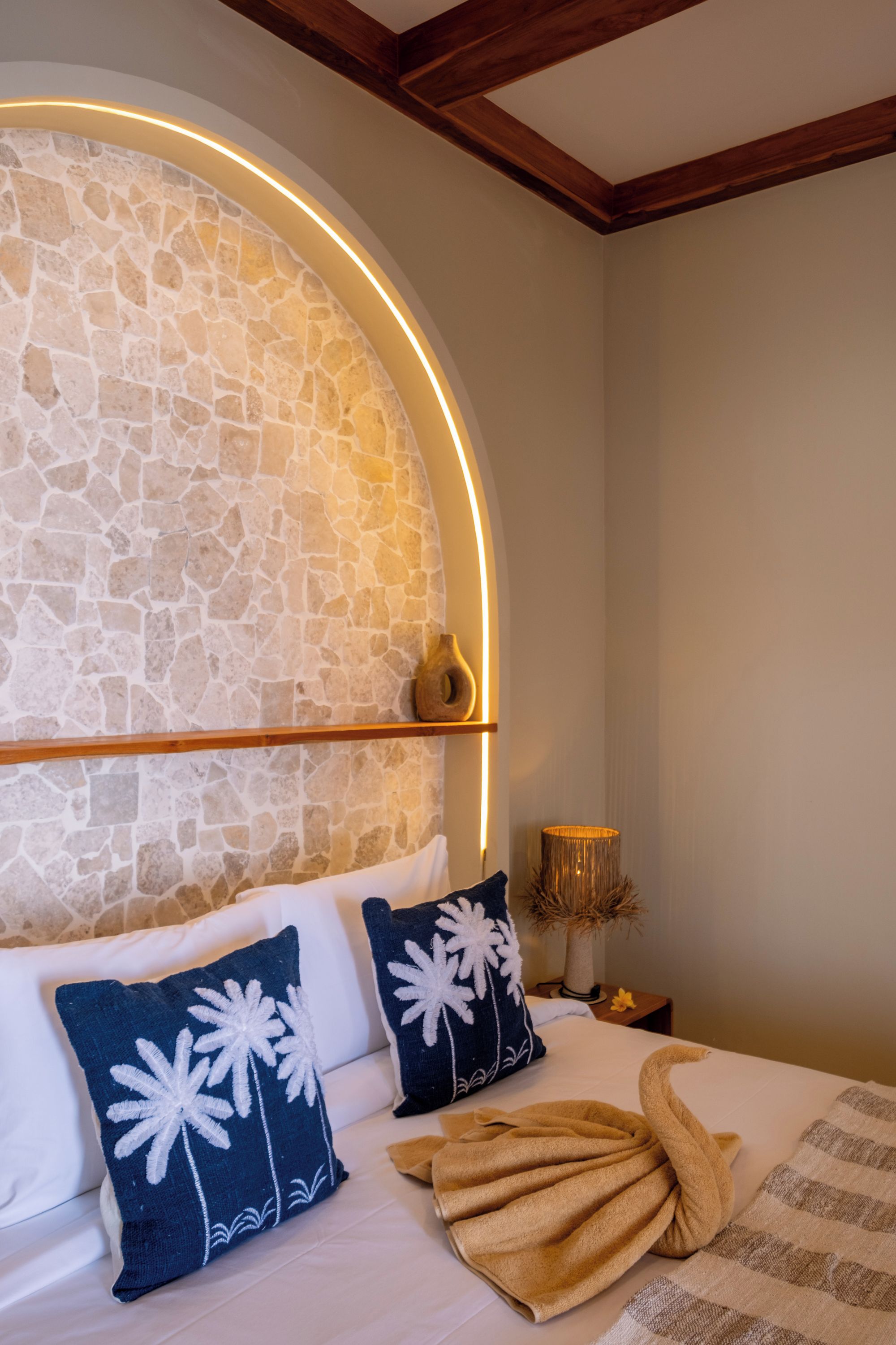 A bedroom with a stone wall, a wooden ceiling, and a bed with white bedding and decorative pillows.