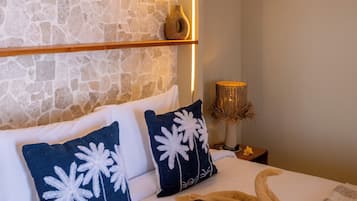 A bedroom with a stone wall, a wooden ceiling, and a bed with white bedding and decorative pillows.