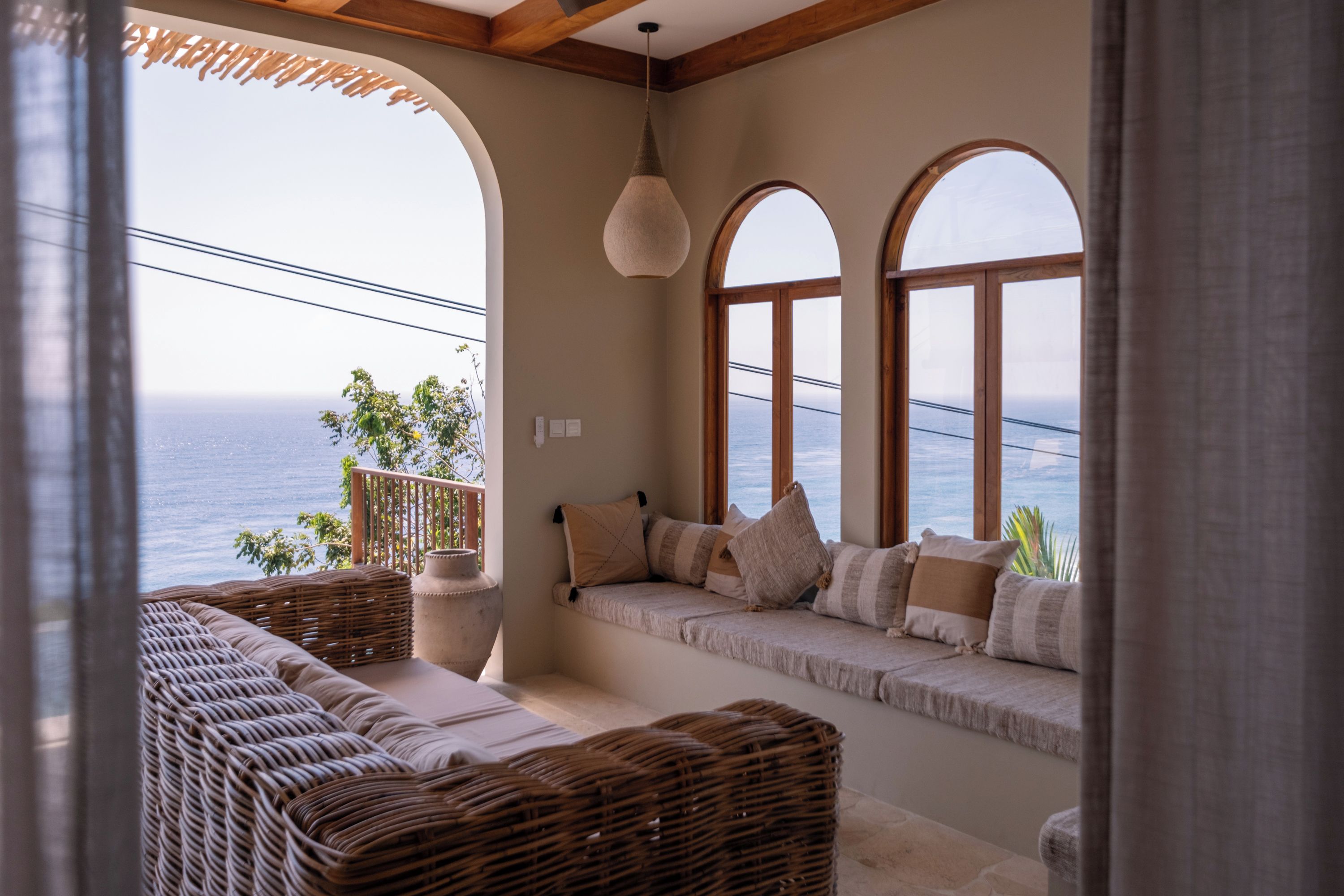 Un balcón con vista al mar, muebles de mimbre y una lámpara colgante.