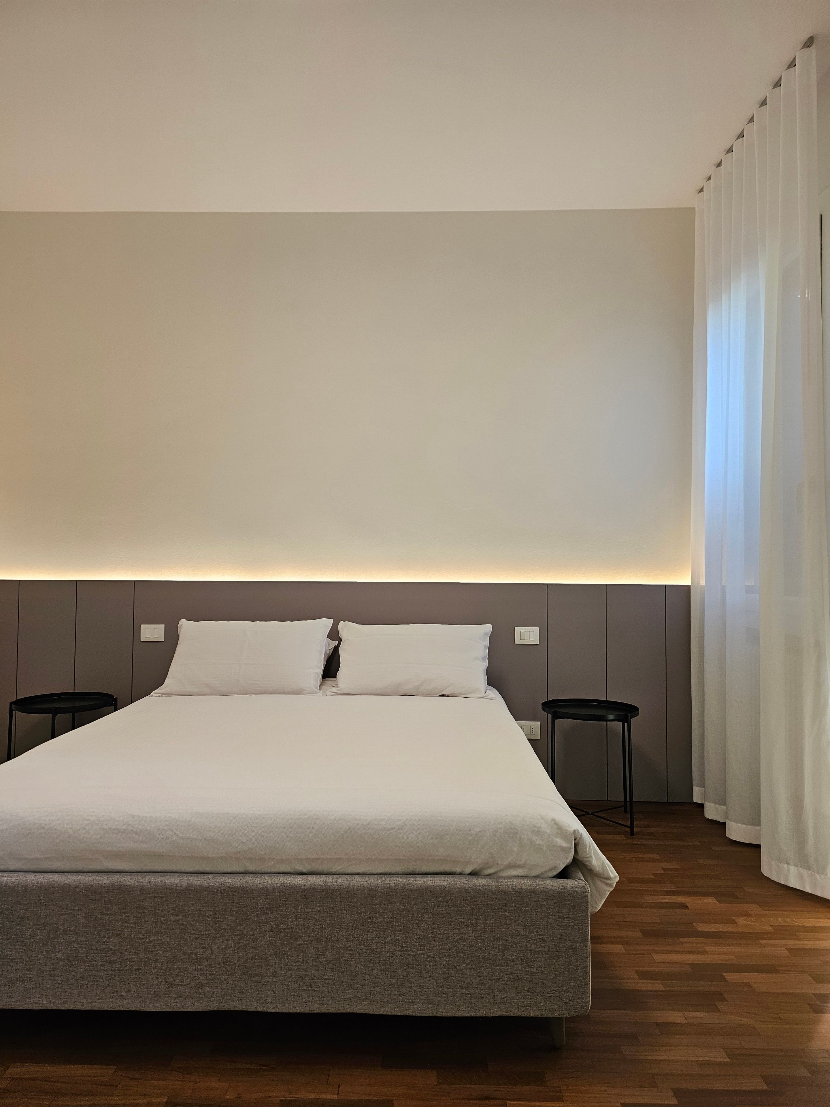 Ein modernes Hotelzimmer mit einem großen Bett, zwei Nachttischen und einem Kopfteil mit integrierter Beleuchtung.