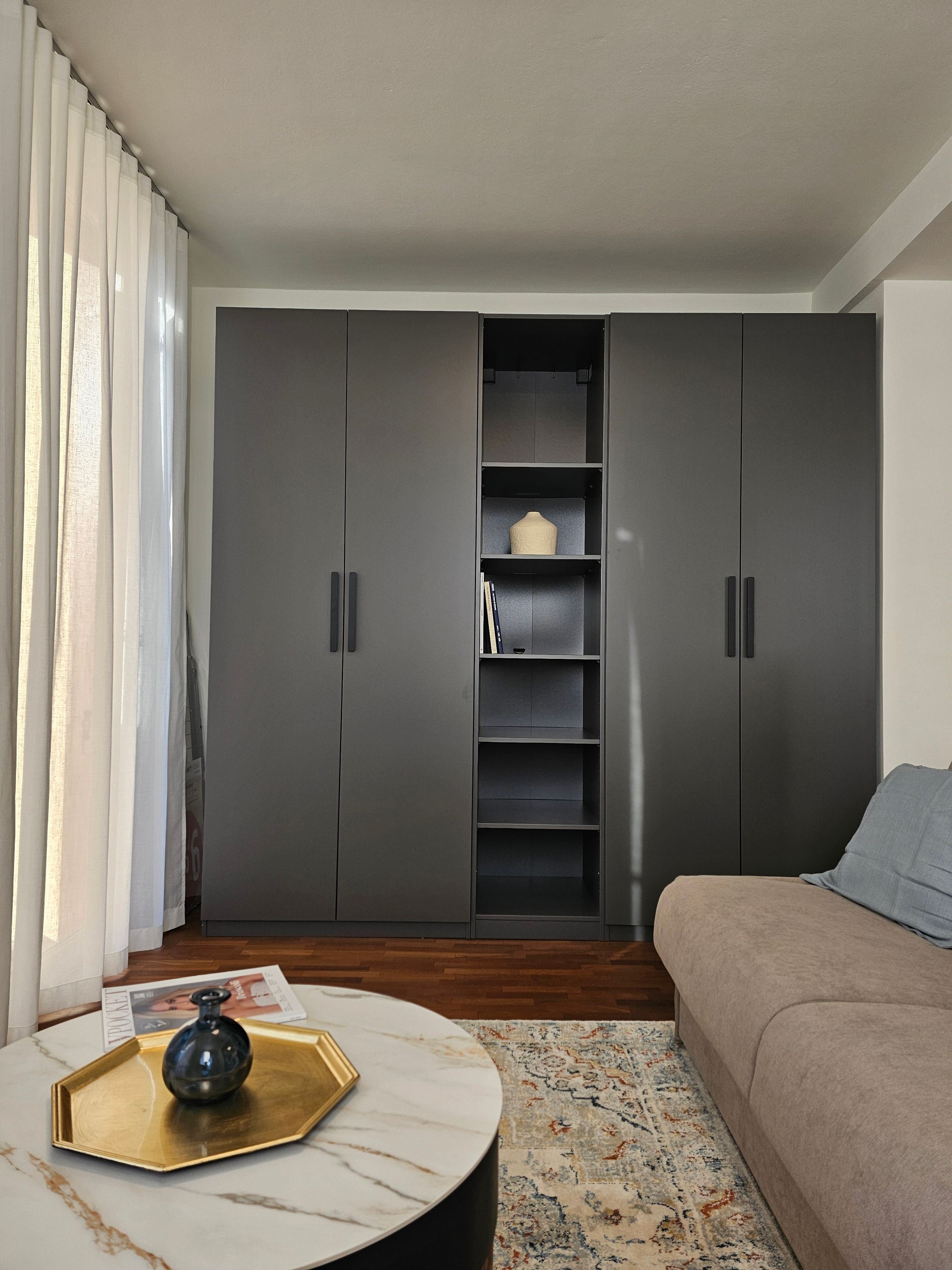Ein modernes Wohnzimmer mit einem grauen Kleiderschrank, einem runden Couchtisch mit einer Dekoration und einem gemusterten Teppich.
