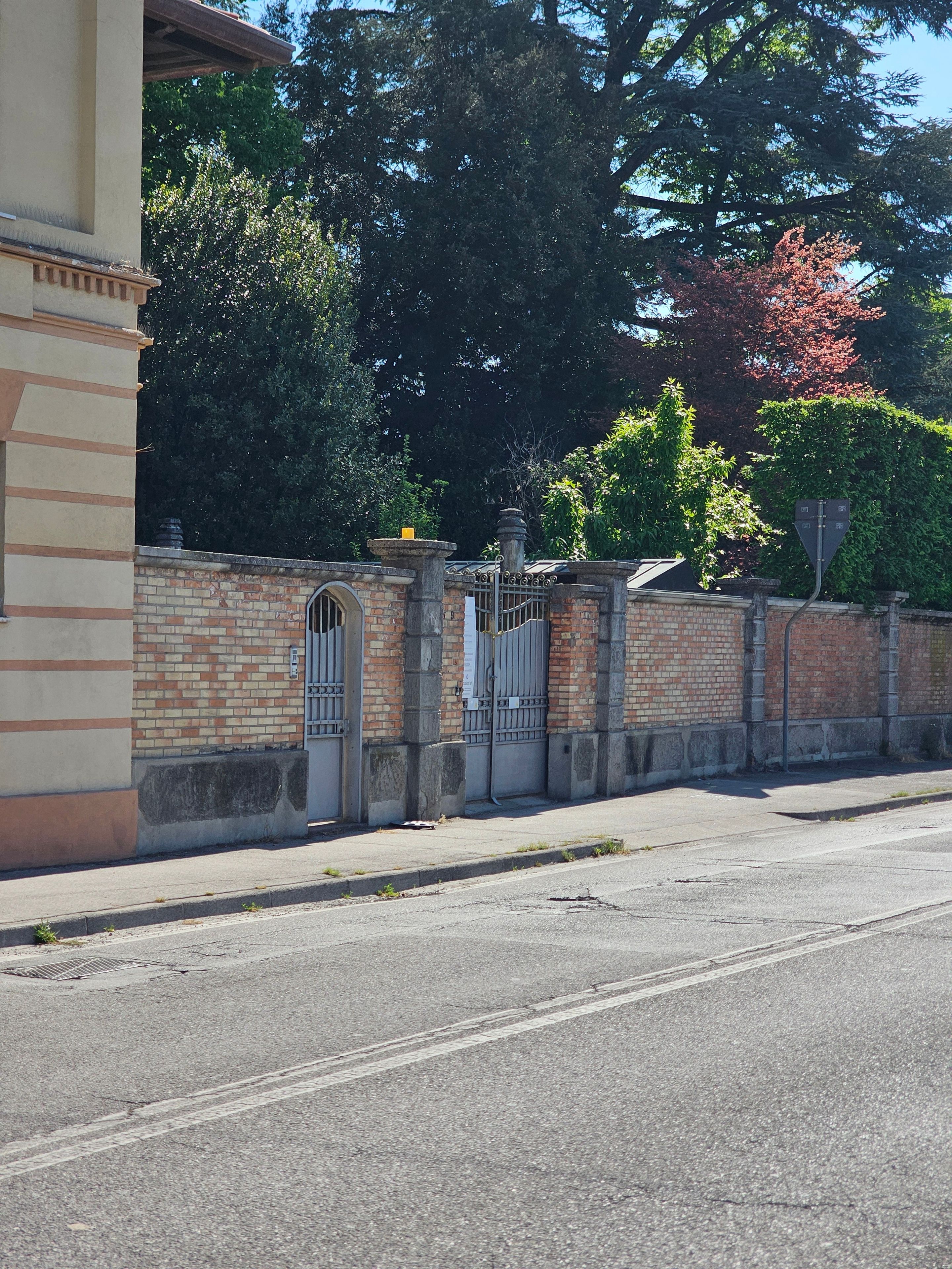 A street view with a brick wall, a metal gate, and a building with a tiled roof.